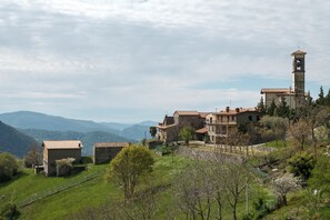 Un pueblo histórico con edificios de piedra, una torre de campanas y montañas al fondo.