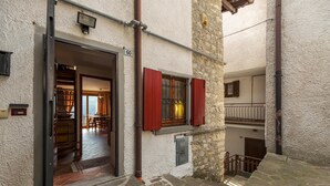 A narrow stone-paved courtyard with a wooden door leading to a room with a tiled floor and a visible staircase. - Casa del Picchio in Adrara San Martino (Adrara San Martino)