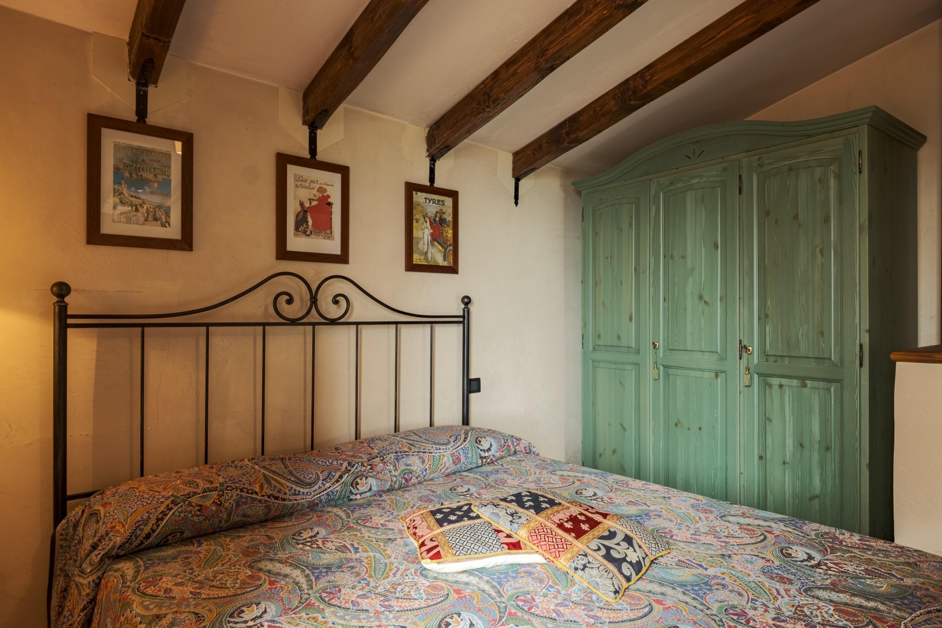 Ein Schlafzimmer mit einem Bett, einem grünen Kleiderschrank und drei gerahmten Bildern an der Wand.