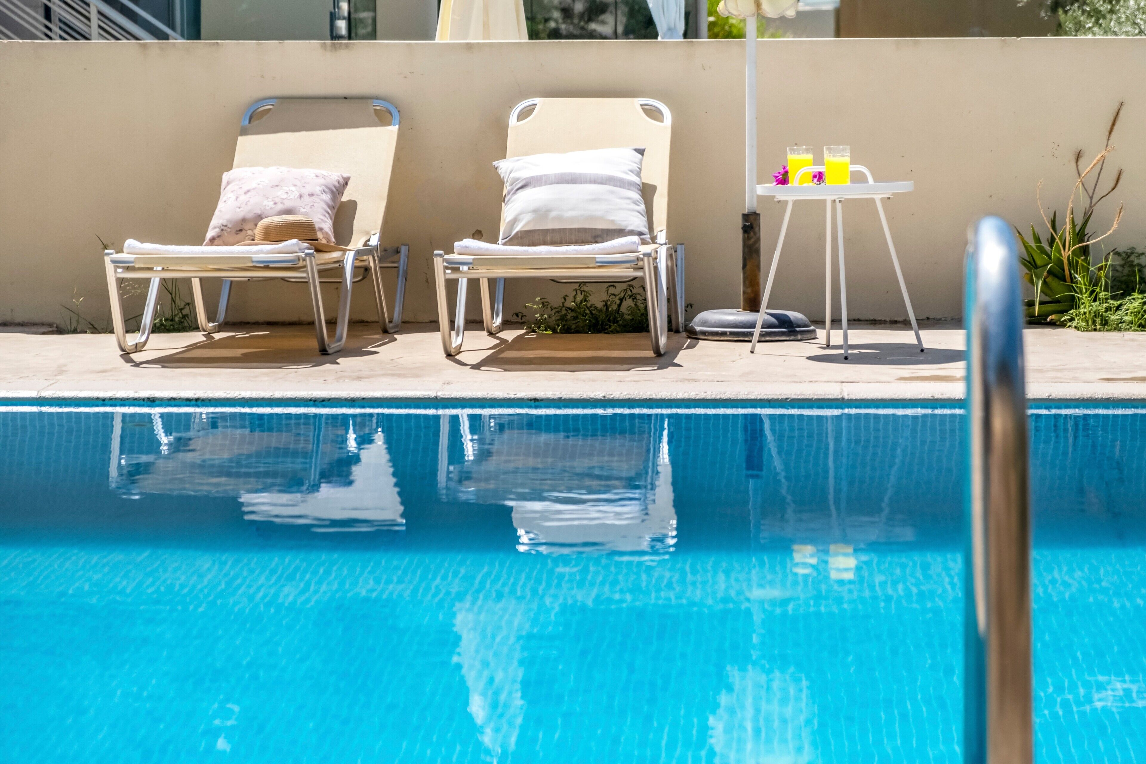 A swimming pool with two lounge chairs and a small table with drinks.