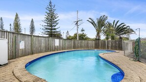 Piscina con valla de madera, rodeada de árboles y cielo despejado.