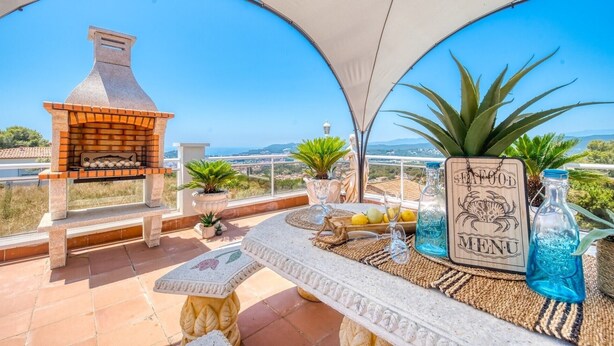 Eine Terrasse mit Backofen, Blumentöpfen, einem Tisch und einer Speisekarte sowie einem schönen Ausblick.