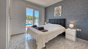 Ein Hotelzimmer mit Bett, Nachttisch, Lampe, einem Gemälde und Blick auf einen Pool.