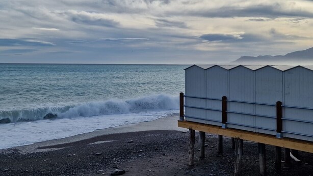 A beach with a wooden structure, waves crashing, and a cloudy sky.