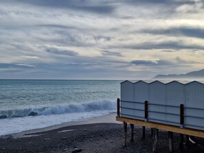 A beach with a wooden structure, waves crashing, and a cloudy sky.