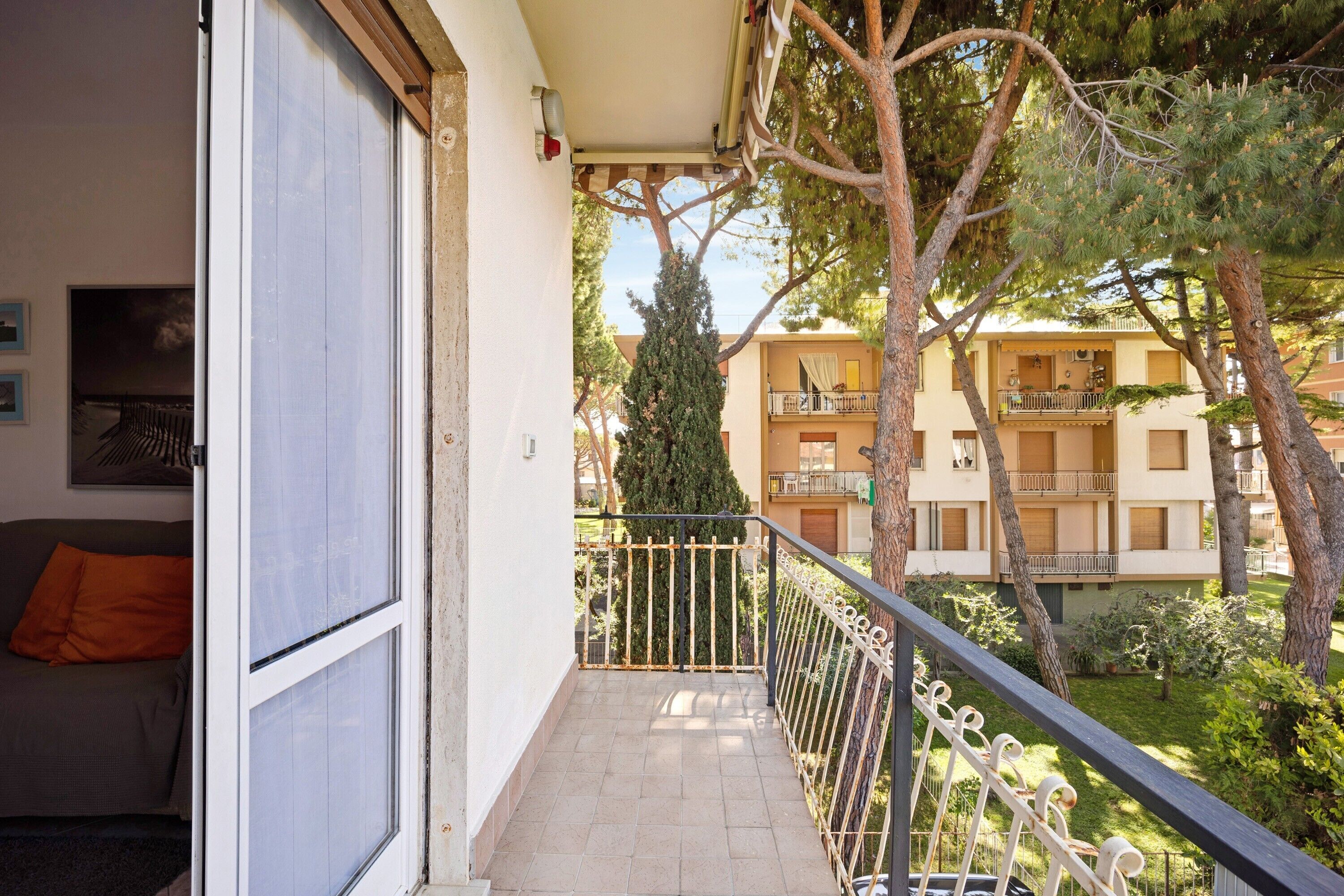 A balcony with a metal railing, a view of a building with balconies, and a tree in the background.