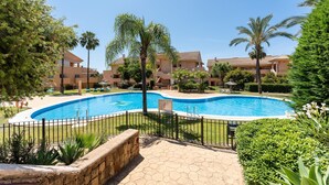 A swimming pool surrounded by a stone fence, palm trees, and a building complex in the background. - Apartment 'Casa Sunchill' with Shared Pool, Wi-Fi and Air Conditioning (Marbella)