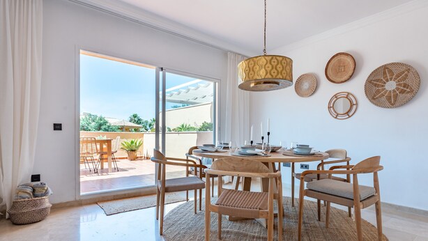 A dining area with a round table, wooden chairs, a woven rug, and a hanging light fixture. - Apartment 'Casa Sunchill' with Shared Pool, Wi-Fi and Air Conditioning (Marbella)