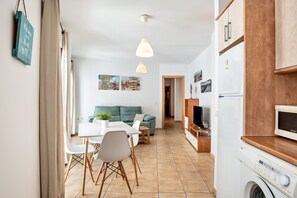 A modern kitchen with a washing machine, a dining area with a table and chairs, and a living room with a sofa and a TV.