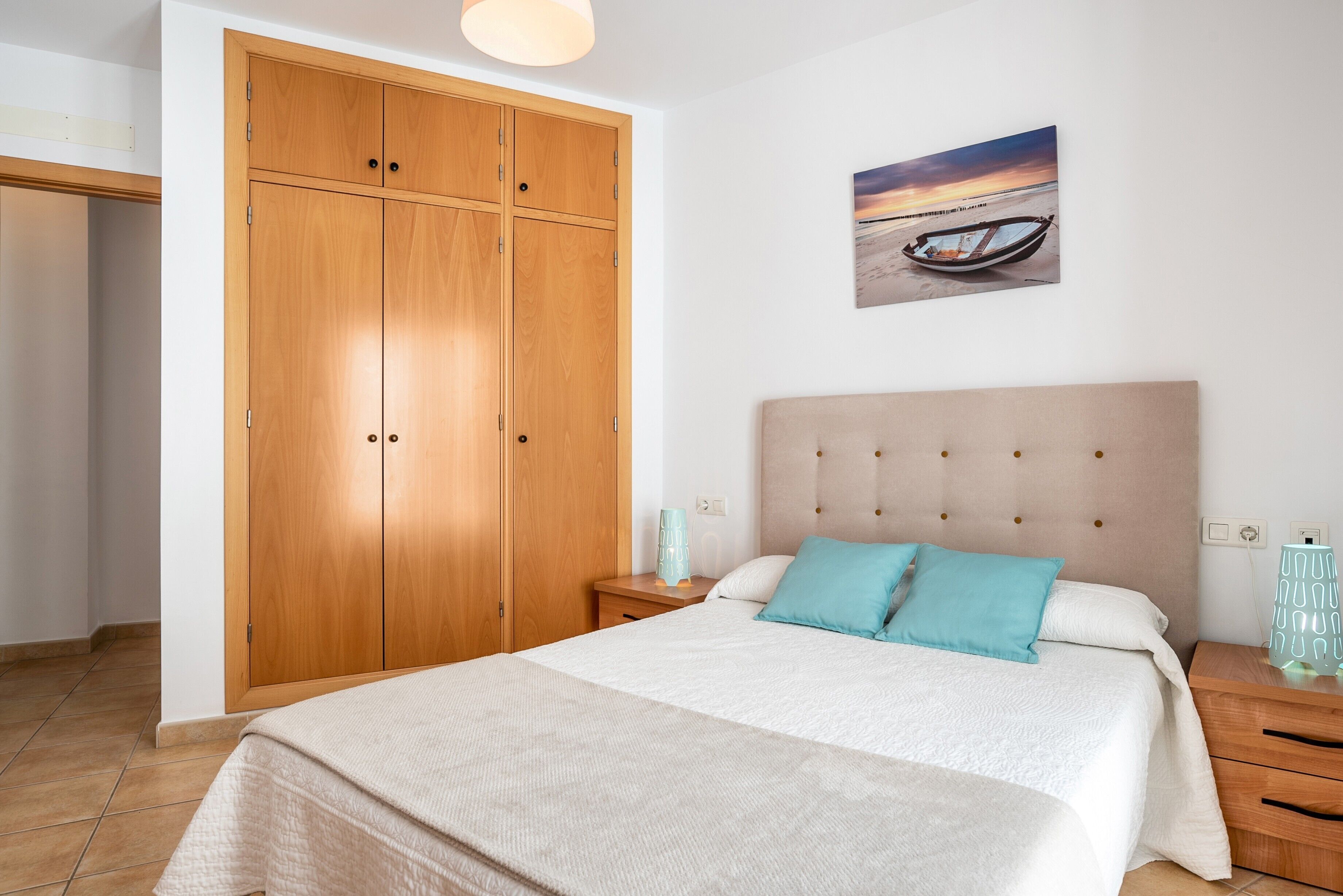 Un dormitorio con cama, mesita de noche, armario de madera y un cuadro en la pared.