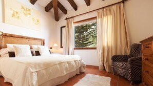 A bedroom with a wooden headboard, a bed with white bedding, a zebra-patterned chair, and a window with curtains. - Villa 'Font' with Mountain View, Wi-Fi and Air Conditioning (Mancor de la Vall)