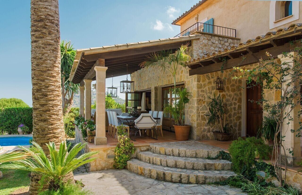 Una casa de piedra con un porche cubierto, mobiliario de exterior y una piscina.