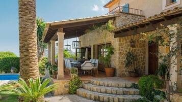 Una casa de piedra con un porche cubierto, mobiliario de exterior y una piscina.