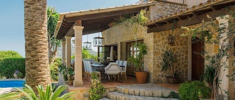 A stone house with a covered patio, outdoor seating, and a pool.