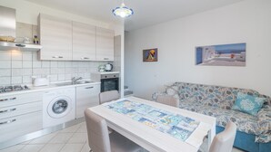 A modern kitchen with a washing machine, dining table, and sofa. - Apartment 'La Gioia' with Sea View, Wi-Fi and Air Conditioning (Palau)