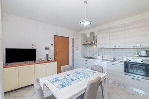 A modern kitchen with a flat-screen TV, a dining table with chairs, and a patterned table runner.