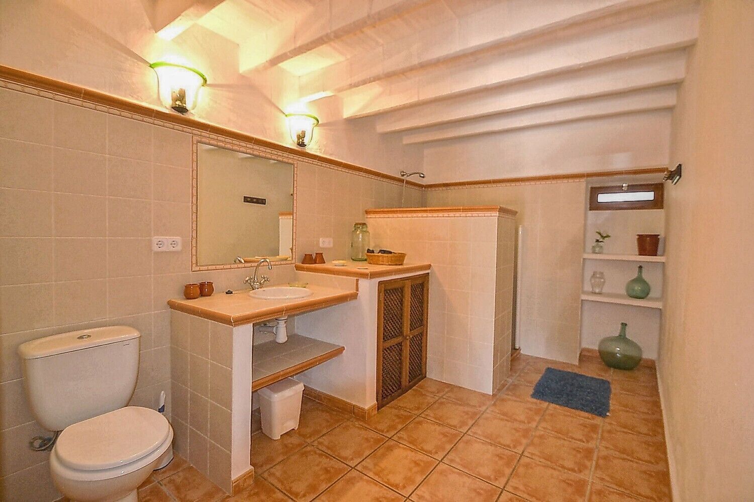 A bathroom with a toilet, sink, mirror, and shelves with toiletries.