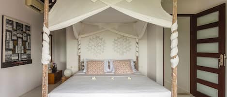 Una cama con dosel y cuatro columnas, con dosel blanco, estructura de madera y dos almohadas estampadas.
