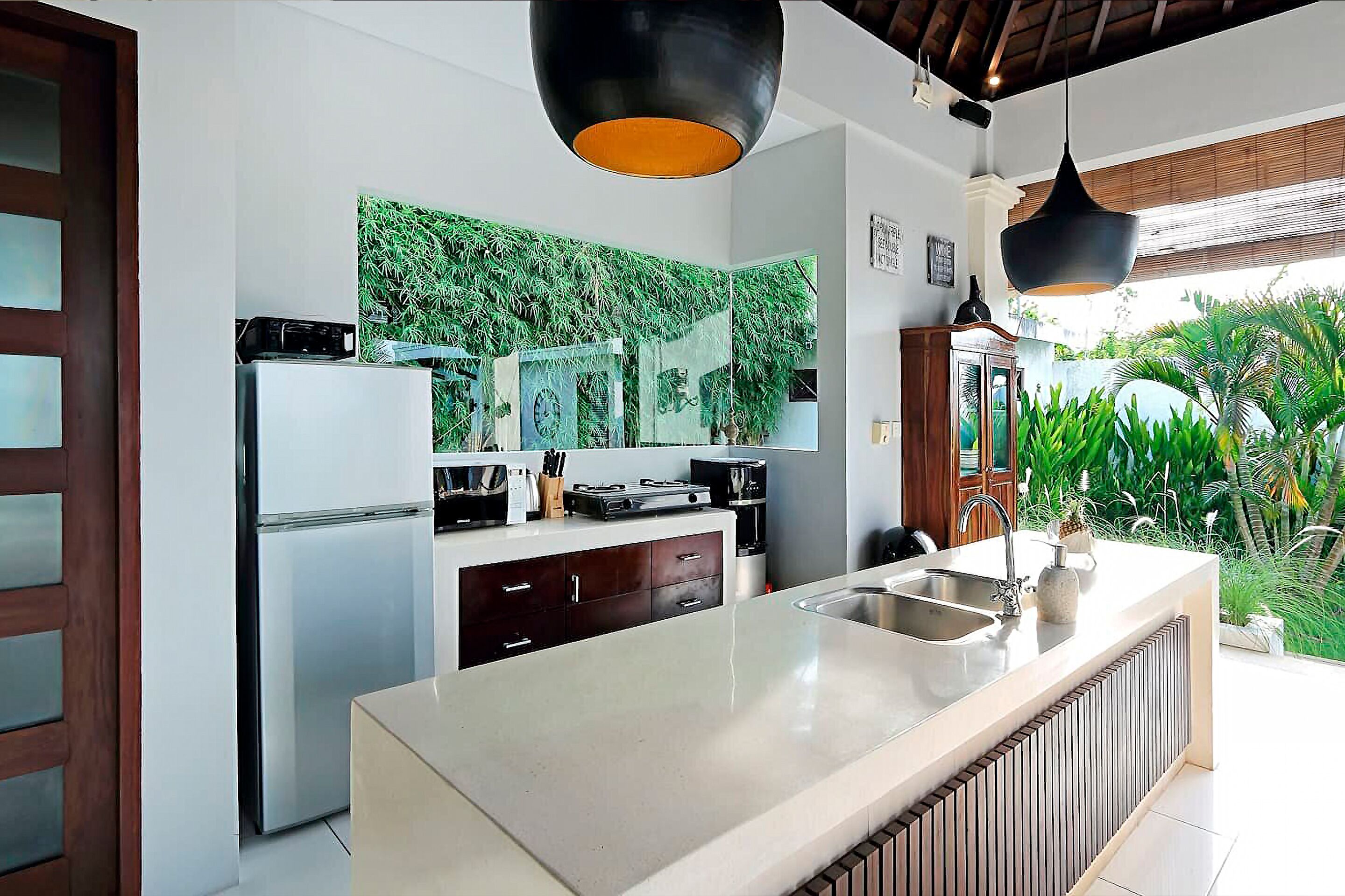 A modern kitchen with a central island, a built-in refrigerator, and a large window overlooking greenery.