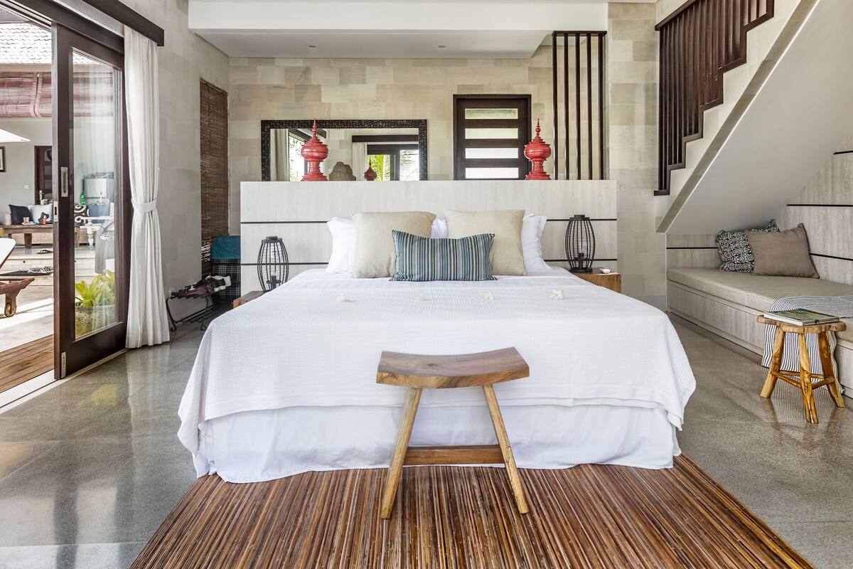 A modern bedroom with a large bed, a wooden stool, and a bench.