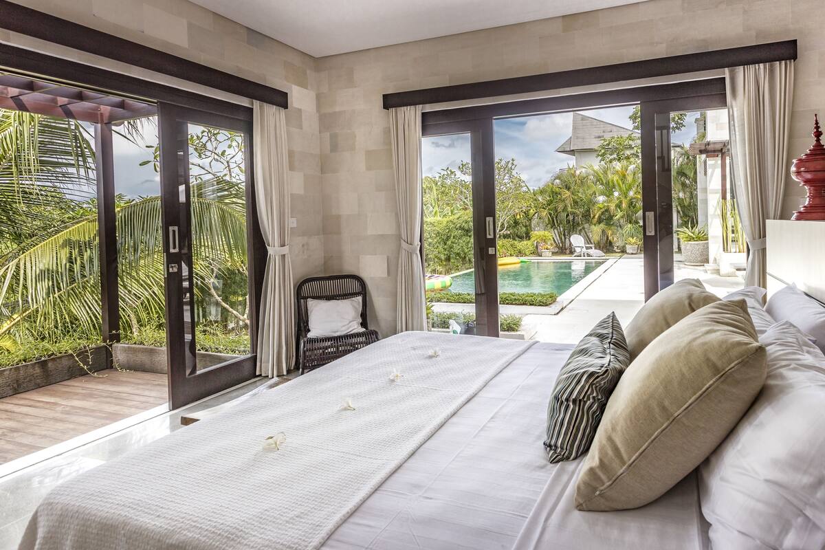 A bedroom with a large bed, a view of a swimming pool, and a chair by the window.