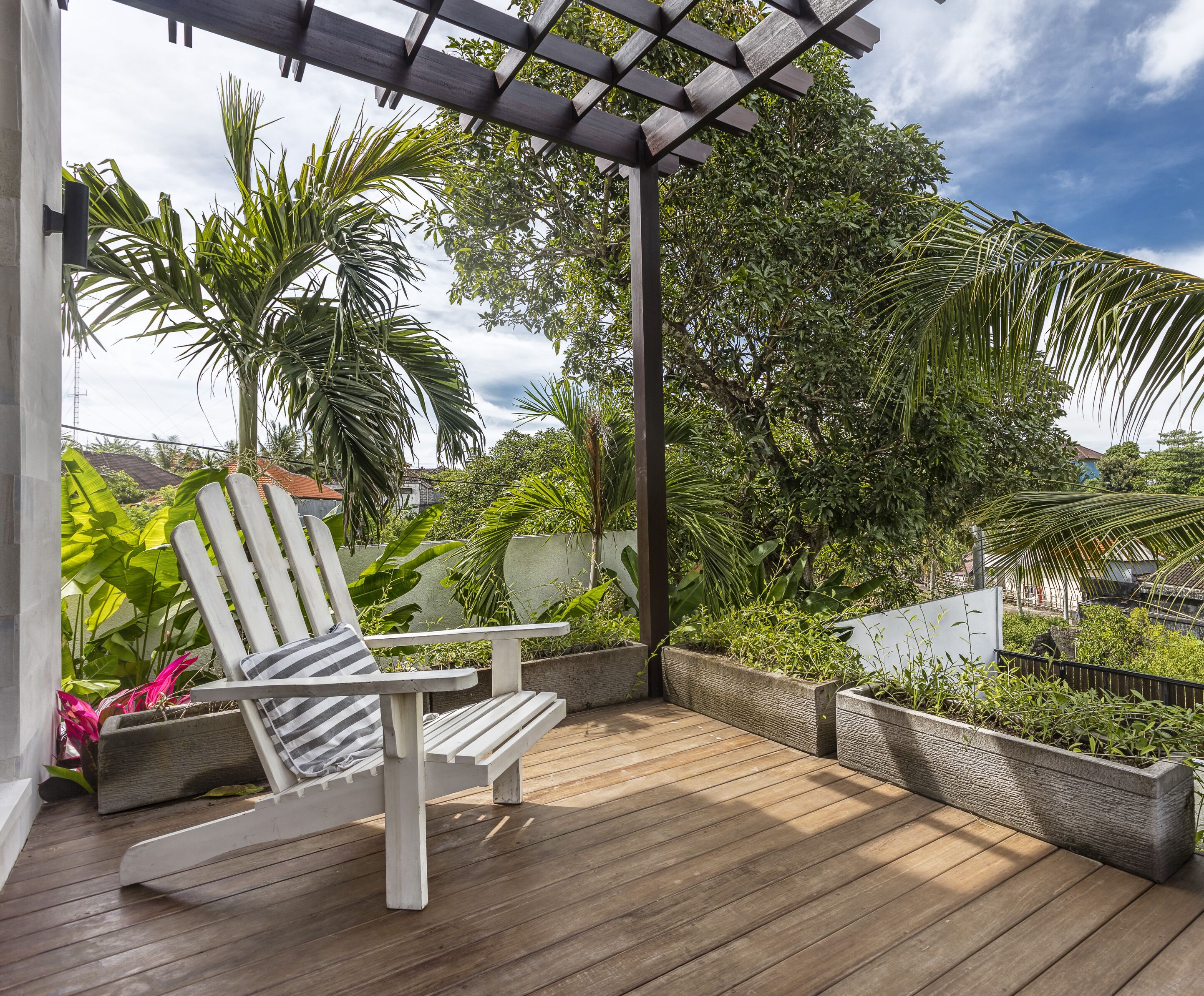 Una terraza de madera con una silla blanca y una pérgola.