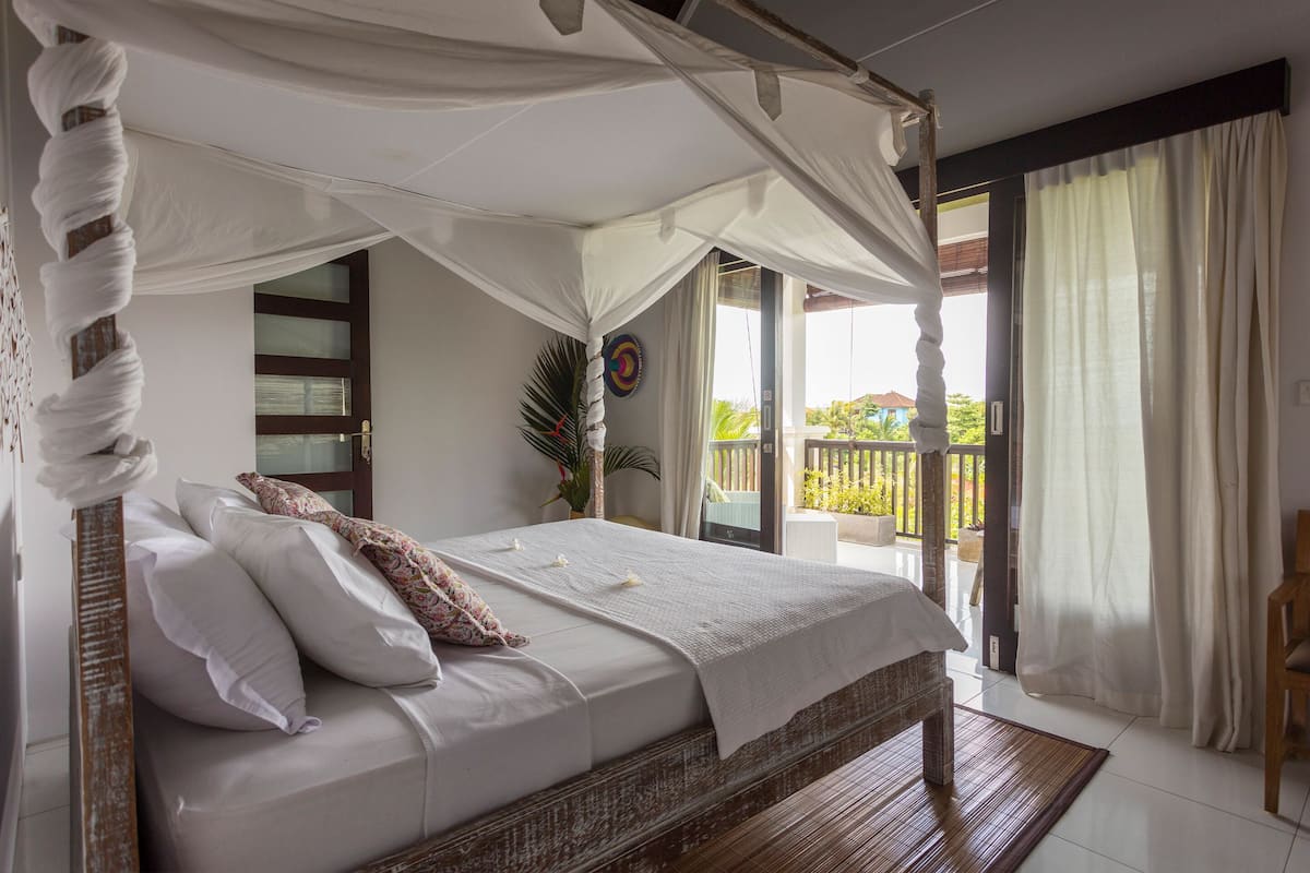 A bedroom with a four-poster bed, a balcony with a view, and a sliding glass door.