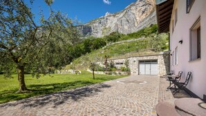 Eine gepflasterte Terrasse mit Steinmuster, ein Steinhaus mit Garage und eine gebirgige Kulisse.