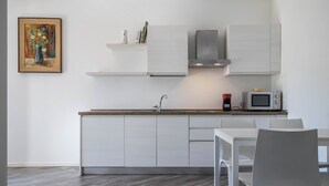 Eine moderne Küche mit weißen Schränken, einer Edelstahl-Dunstabzugshaube, einer Mikrowelle und einem Essbereich mit einem weißen Tisch und Stühlen.