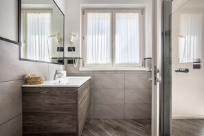 Ein modernes Badezimmer mit einem Holzwaschtisch, einem großen Spiegel, einem Haartrockner und einem Fenster mit Vorhängen.