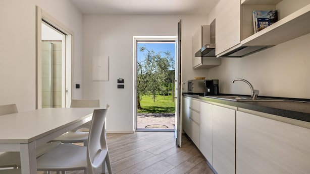 A modern kitchen with a dining area, a view of a green landscape, and a door leading outside. - Studio 'Monte Brento Gaggiolo 2' with Mountain View and Private Garden (DRO)
