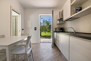 Une cuisine moderne avec un coin repas, une vue sur un paysage verdoyant et une porte donnant sur l’extérieur.