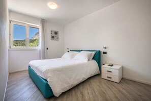Une chambre à coucher comprenant un lit, une table de chevet, une fenêtre avec des rideaux et un luminaire fixé au mur.