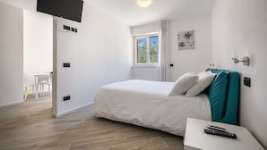 A bedroom with a bed, a TV mounted on the wall, a window with curtains, and a bedside table with a remote control. - Studio 'Monte Brento Gaggiolo 2' with Mountain View and Private Garden (DRO)