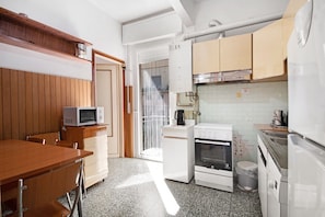 A compact kitchen with a microwave, oven, and sink, wooden cabinets, and a tiled backsplash.