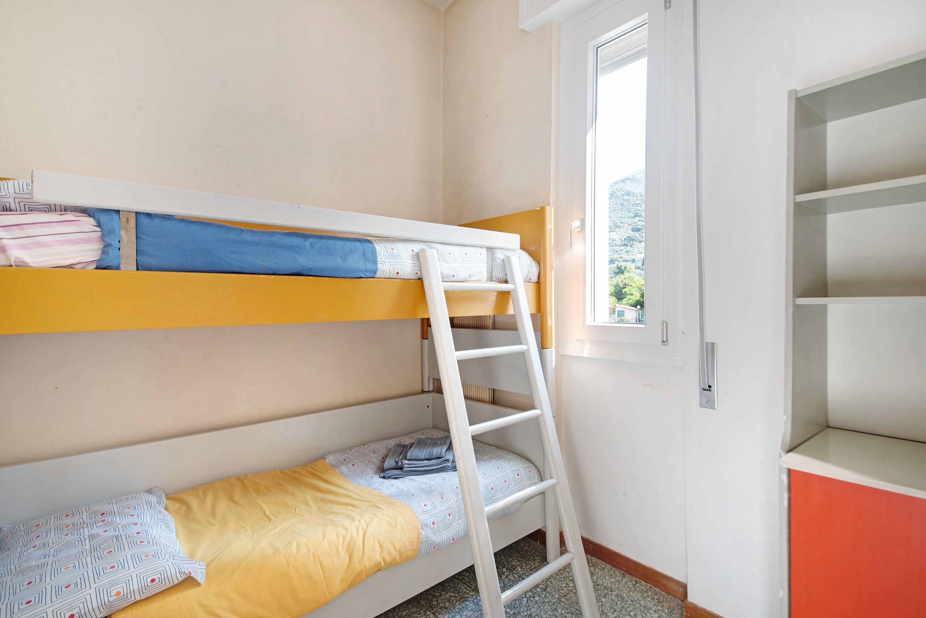 A bunk bed room with a ladder, a window with a view, and a white wardrobe.