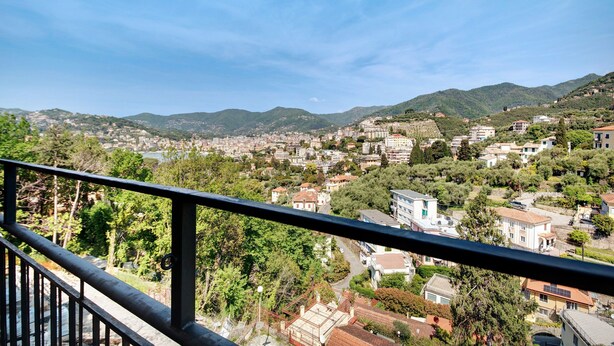 Ein Balkon mit Blick auf eine Hügelstadt, mit Gebäuden, Bäumen und blauem Himmel.