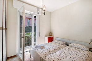 A bedroom with a bed, a nightstand, a lamp, and a balcony door.