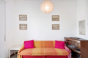 A room with a sofa, framed pictures on the wall, a map, and a lamp.