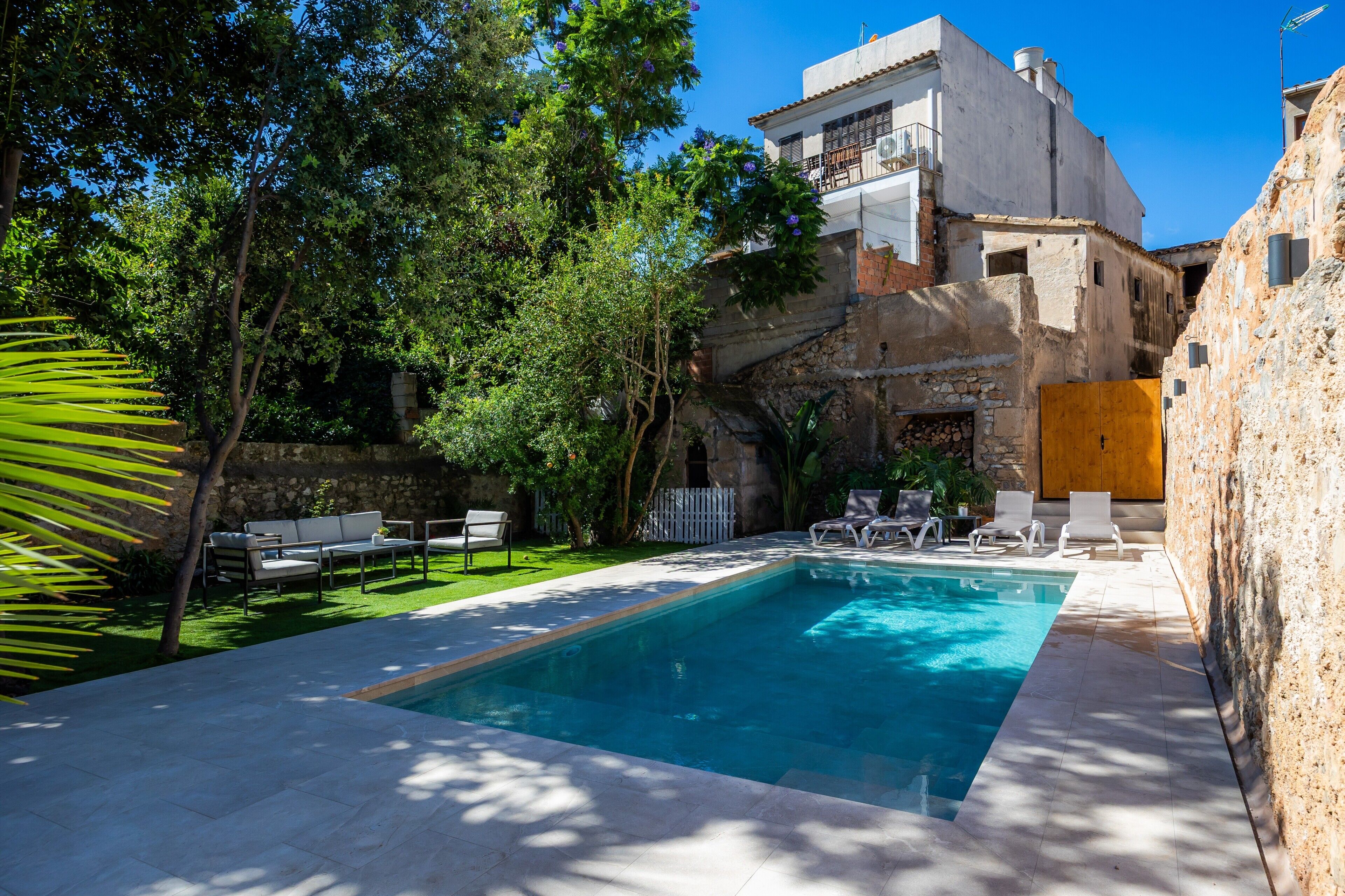 Una piscina amb gandules, un mur de pedra i un edifici amb balcons.
