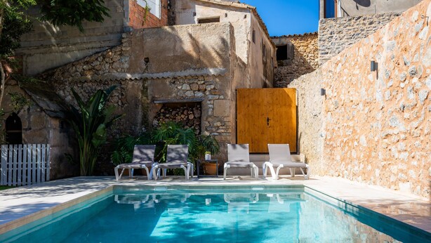 A swimming pool with lounge chairs, a wooden door, and stone walls. - Holiday Home 'Ca La Senyora Dels Arbres' with Private Pool, Terrace and Wi-Fi (Arta)