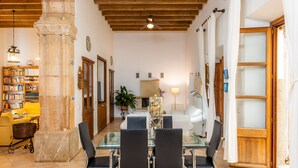 A dining area with a glass table, black chairs, a wooden ceiling, a stone pillar, and a bookshelf. - Holiday Home 'Ca La Senyora Dels Arbres' with Private Pool, Terrace and Wi-Fi (Arta)