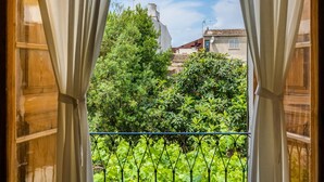 A view through curtains of a balcony with a metal railing, surrounded by lush greenery and buildings in the background. - Holiday Home 'Ca La Senyora Dels Arbres' with Private Pool, Terrace and Wi-Fi (Arta)