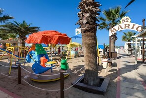 A beach area with a children's play area, including a carousel and swings, and a sign reading '52 MARIO'.