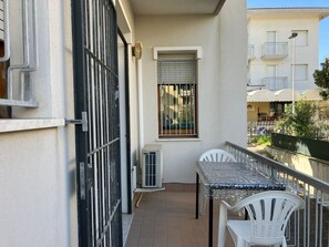 Un balcone con tavolo e sedie, una finestra con ringhiere e un edificio con balconi sullo sfondo.
