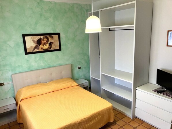 Une chambre à coucher comprenant un lit, une table de chevet, une télévision, une armoire et un luminaire suspendu.