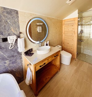 Un baño moderno con pared de mármol, tocador de madera, espejo redondo, bañera y cabina de ducha de cristal.