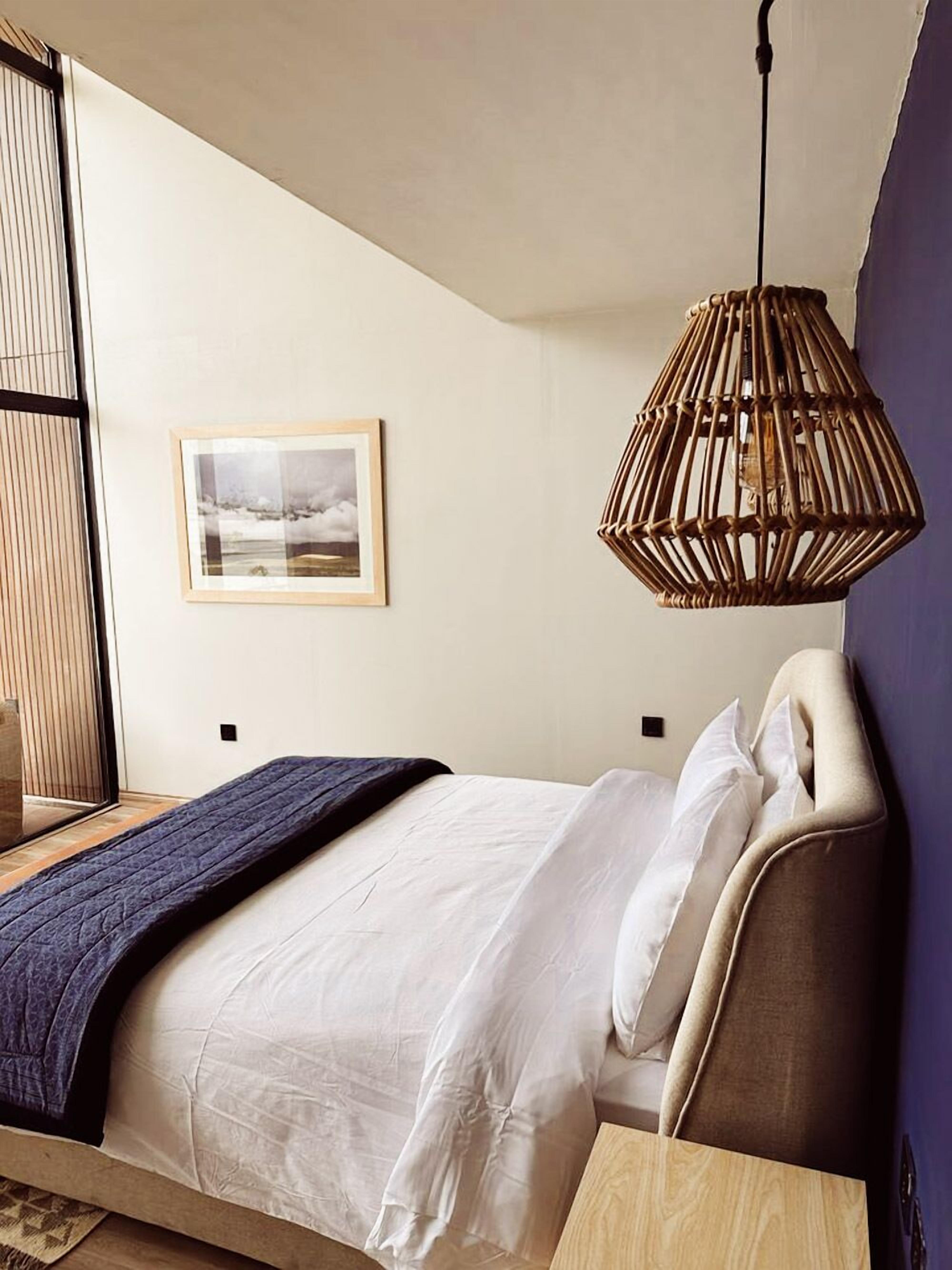A modern bedroom with a bed, a hanging rattan light fixture, and a framed picture on the wall.