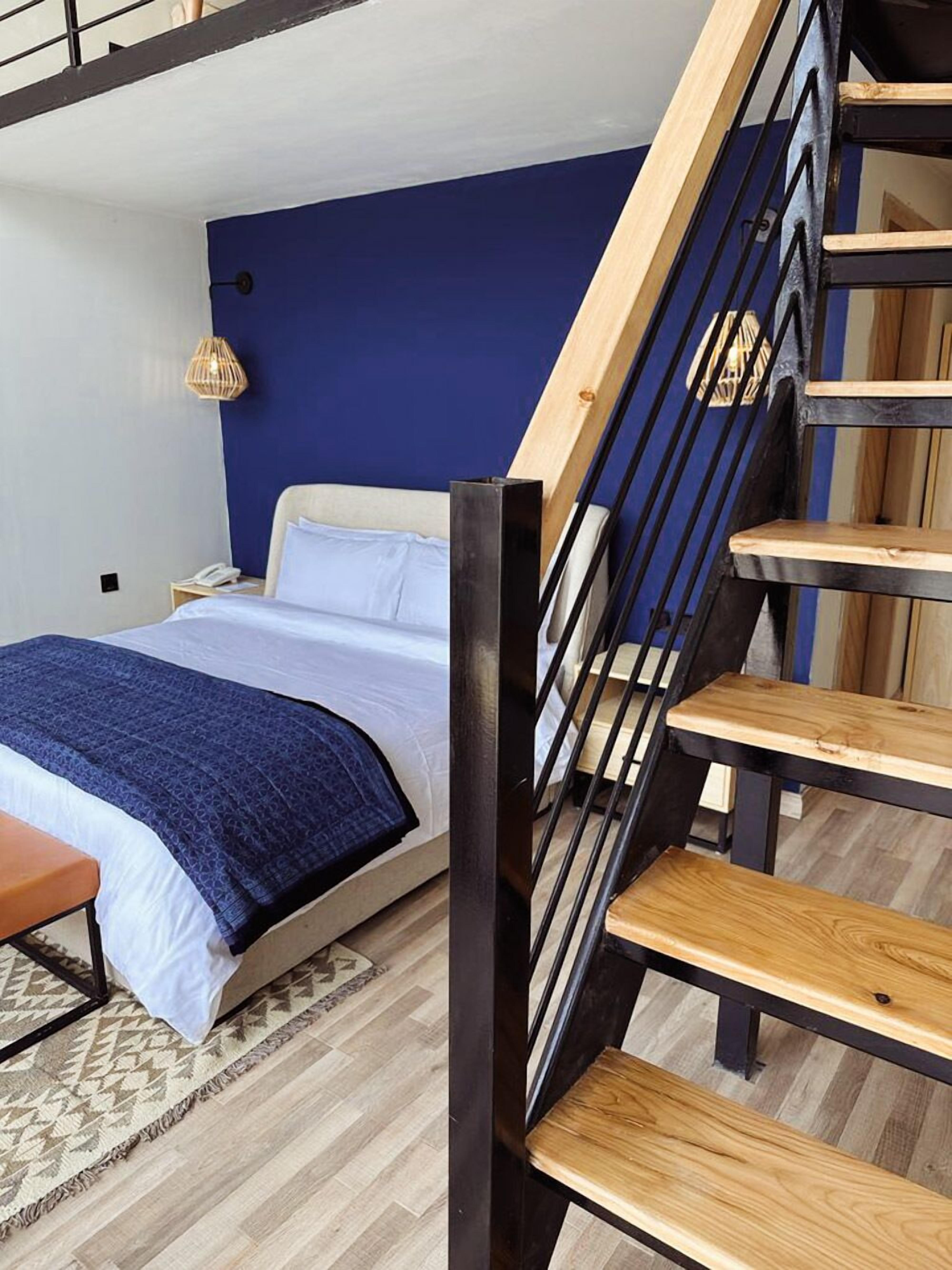 A bedroom with a bed, a wooden staircase, and a blue accent wall.