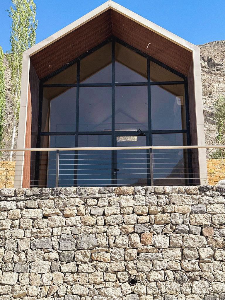 Un edificio moderno con base de pared de piedra, ventanas amplias y techo de madera.
